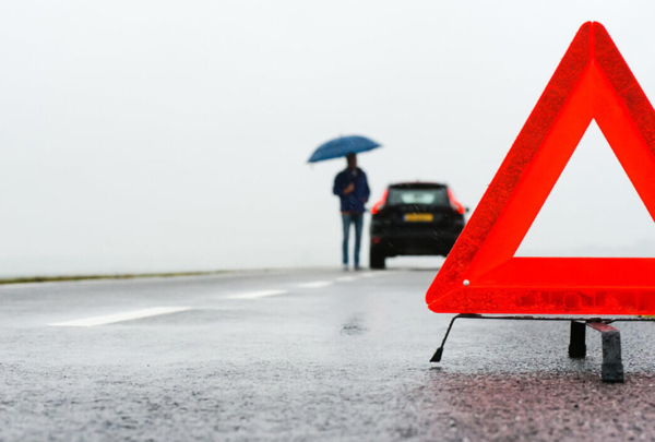 Person standing by broken down car on the side of the road.