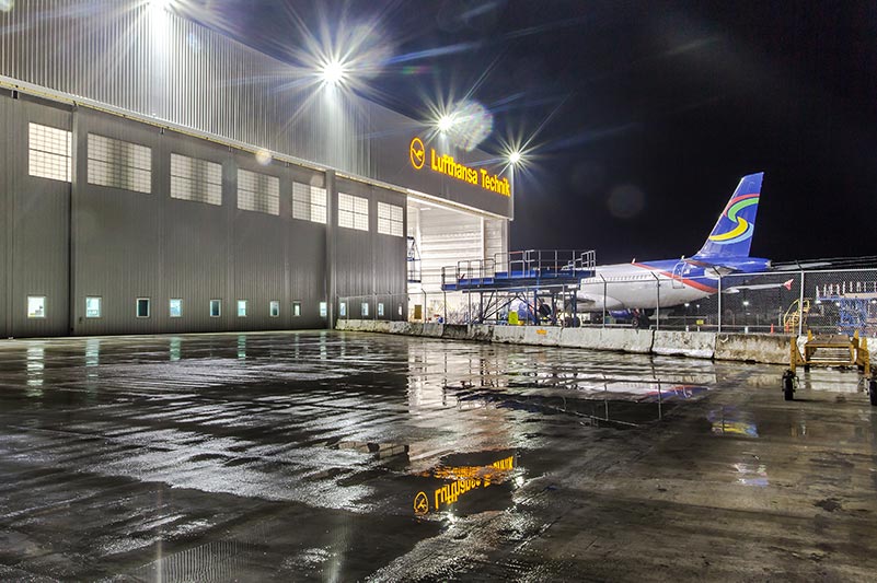 Exterior of Lufthansa Technik Heavy Maintenance Facility at night. Airplane entering hangar in the back.