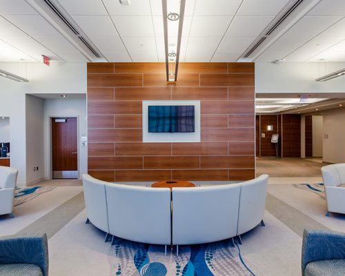 Interior photo of a lounge with cream colored couches in front of wood paneled wall with a television.