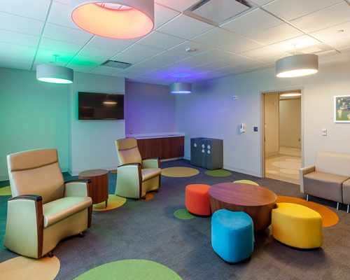 Interior photo of lounge area with colorful lighting, carpeting and seating. Couches line the wall.