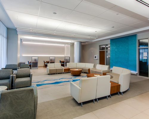 Interior photo of a waiting area. Cream colored chairs are in a U shape in the center of the room.