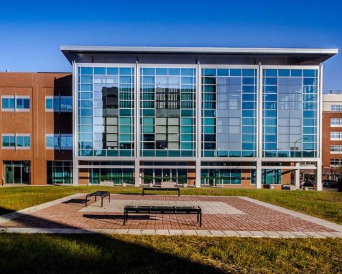 Exterior photo of Maryland Proton Treatment Center during the day. Brick patio with benches are in the middle or a grassy area.