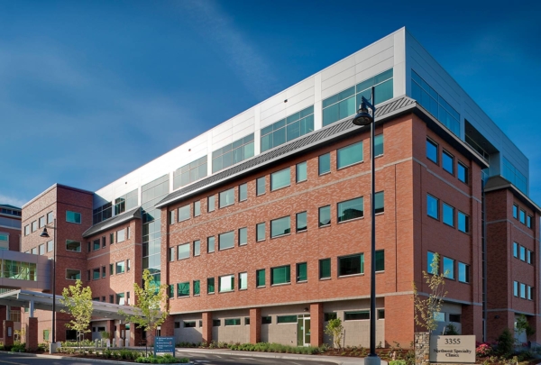 Exterior photo of the entrance at Northwest Specialty Center. Five level, red brick structure against bright blue skies. Newly installed landscaping surrounds facility.